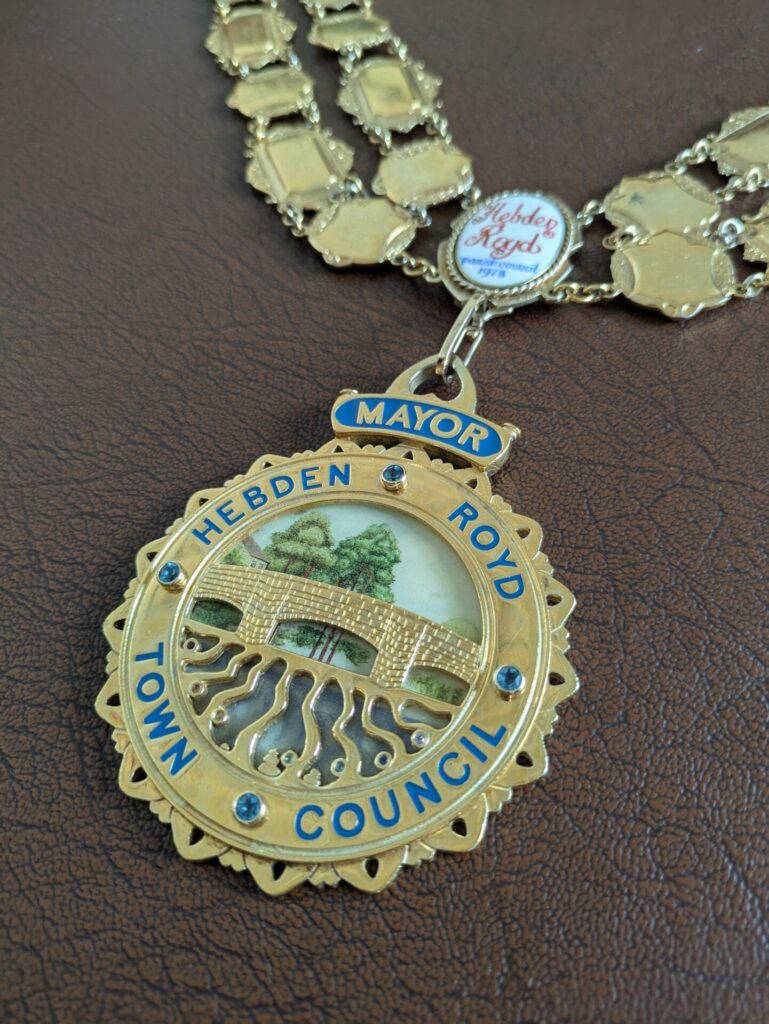 Photograph of a close up of the Mayoral chain. The design is gold showing a bridge over a flowing river.
