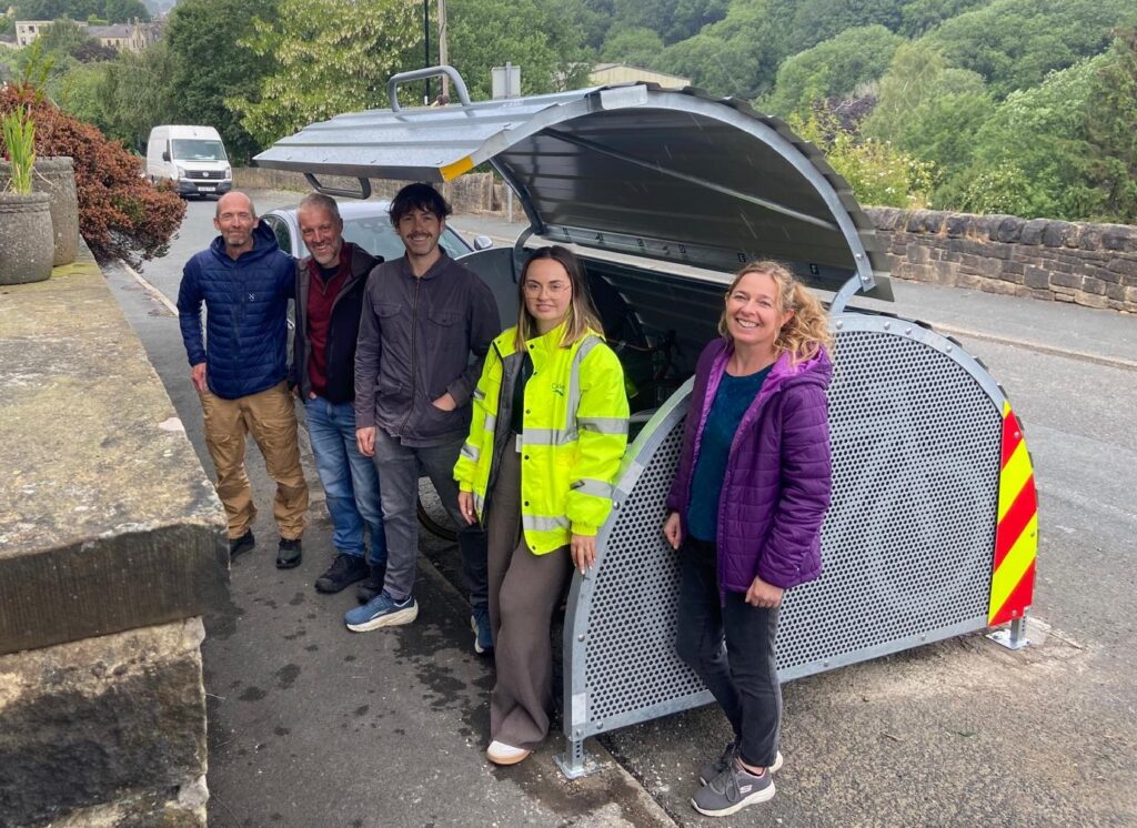 Councillors from HRTC and CMBC standing beside a new bike hangar in Mytholmroyd