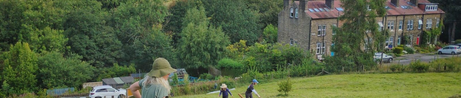 Haytime 2025 adults and children raking hay onto a tarpaulin with Pecket Well mill on the horizon