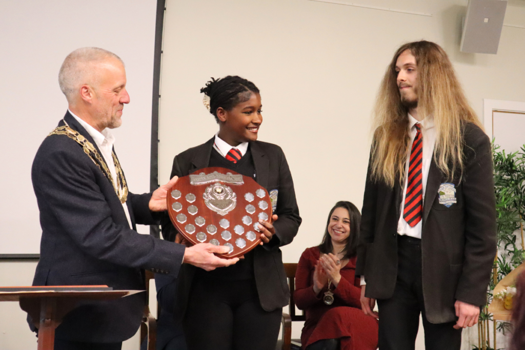 Cllr Woodhead (left) presents Lucia, the Prime Minister (middle) and Jude, the Deputy Prime Minister (right), with the Service to the Community Award shield and certificate.