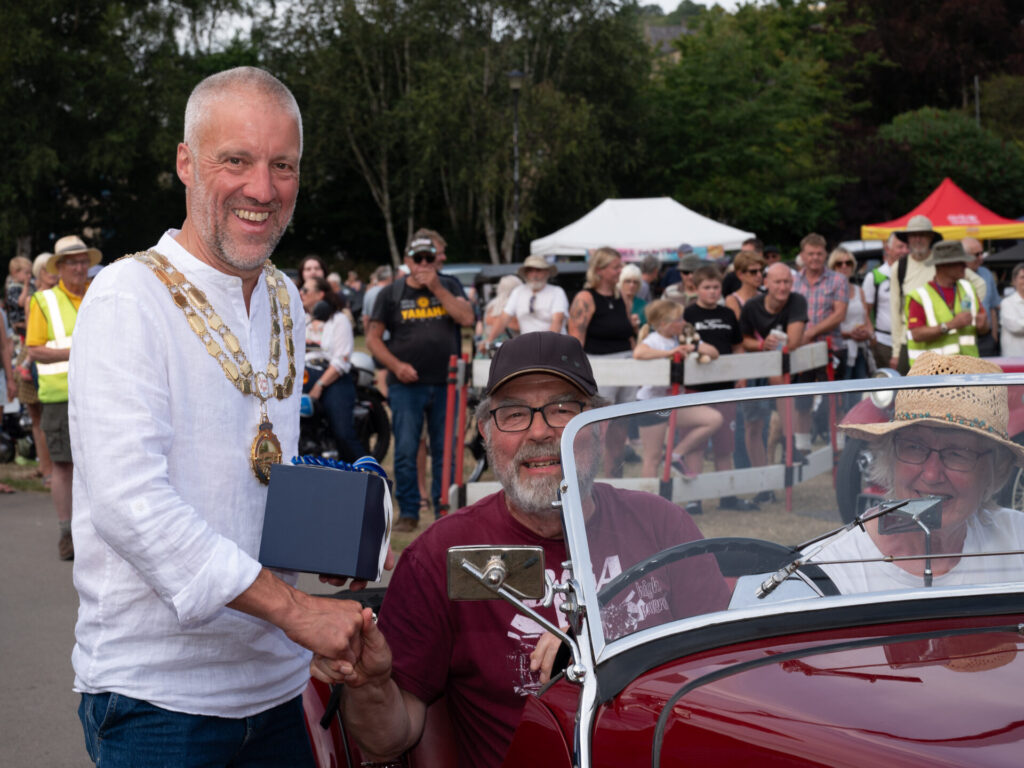 The Mayor of Hebden Royd Town Council hands a prize to a driver sat in a vintage car, at the Hebden Bridge Vintage Weekend.