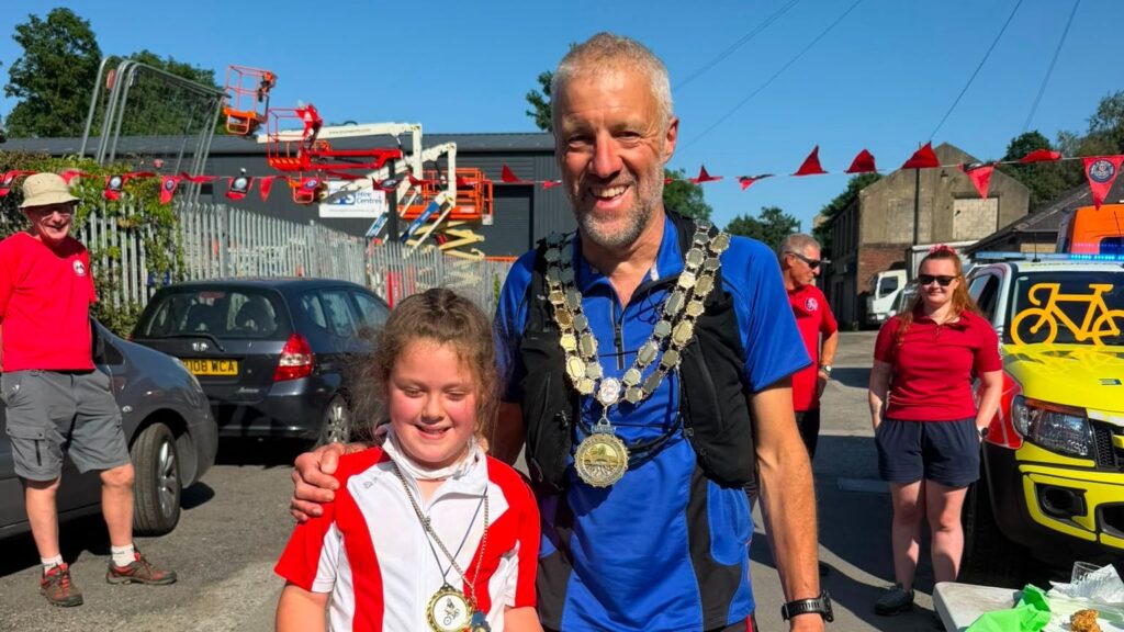 The Mayor of Hebden ROyd Town Council, CLlr Steve Woodhead, stands next to his Consort and granddaughter WInnie Woodhead, at the finish line of their 60-mile charity cycle between Mytholmroyd and Manchester.